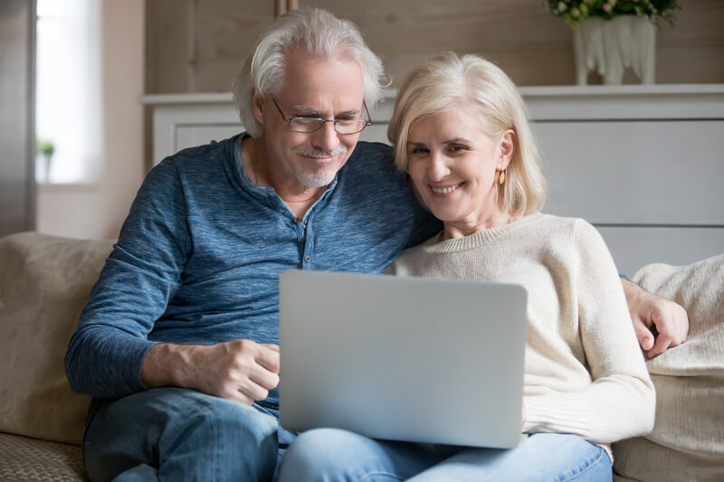 An older couple smiling at a laptop on the sofa