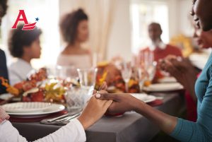 Young black adult woman and her daughter holding hands and saying grace with their multi generation family at the Thanksgiving din. Young black adult women and her daughter holding hands and saying grace with their multi generation family at the Thanksgiving dinner table, detail, focus on foreground